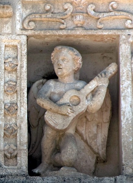Façade niche sculpture, musician youth (right) - Façade, exterior buttressing, lateral portal, open & posa chapels, atrio & cross