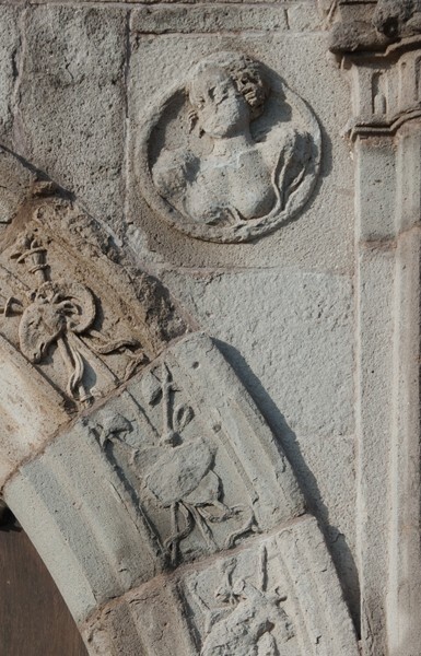 N portal, right spandrel roundel relief - San Juan Bautista, façade, portería & posa chapels