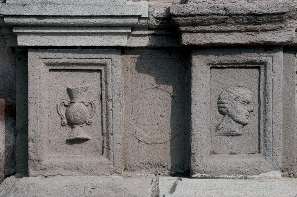 Façade portal, left pillar base reliefs - San Juan Bautista, façade, portería & posa chapels