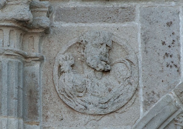 N portal, left spandrel roundel relief - San Juan Bautista, façade, portería & posa chapels