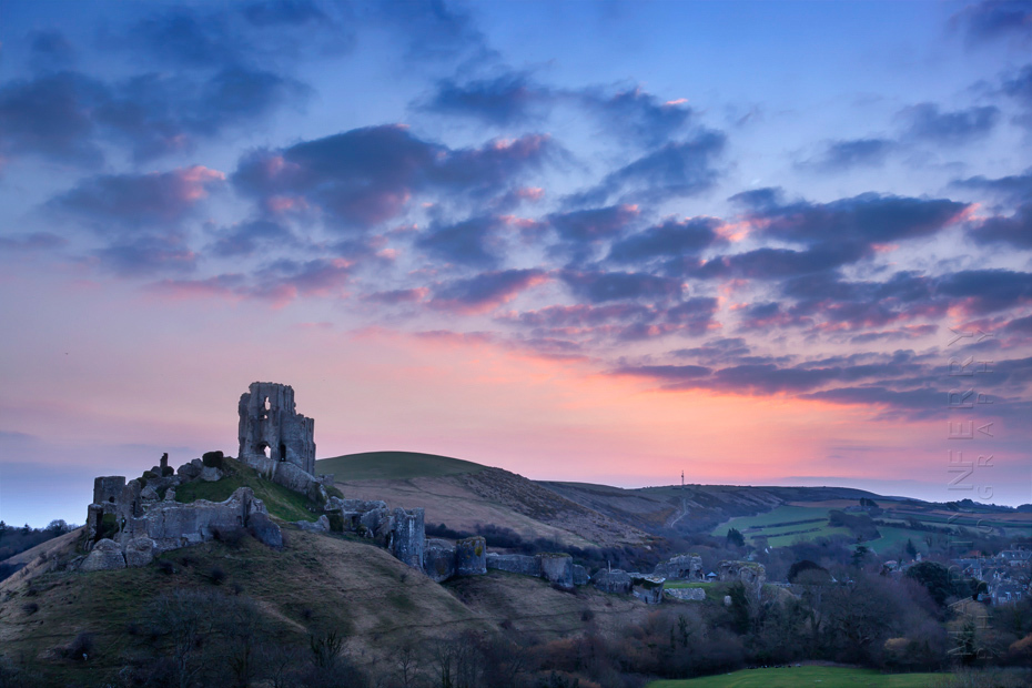 Warm glow of dawn lights up the sky behind Corfe Castle