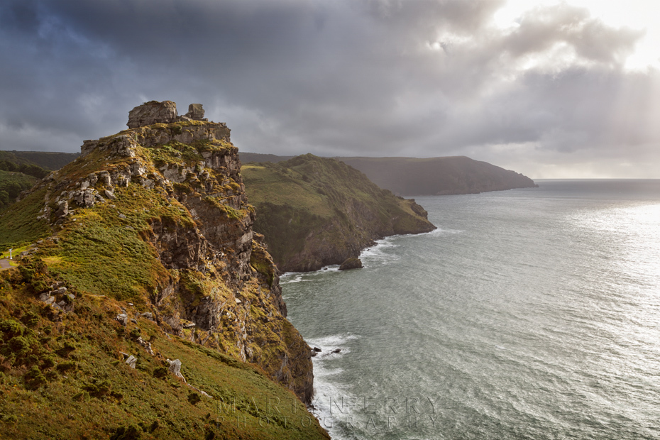 Castle Rock lit up by the evening sun under stormy clouds