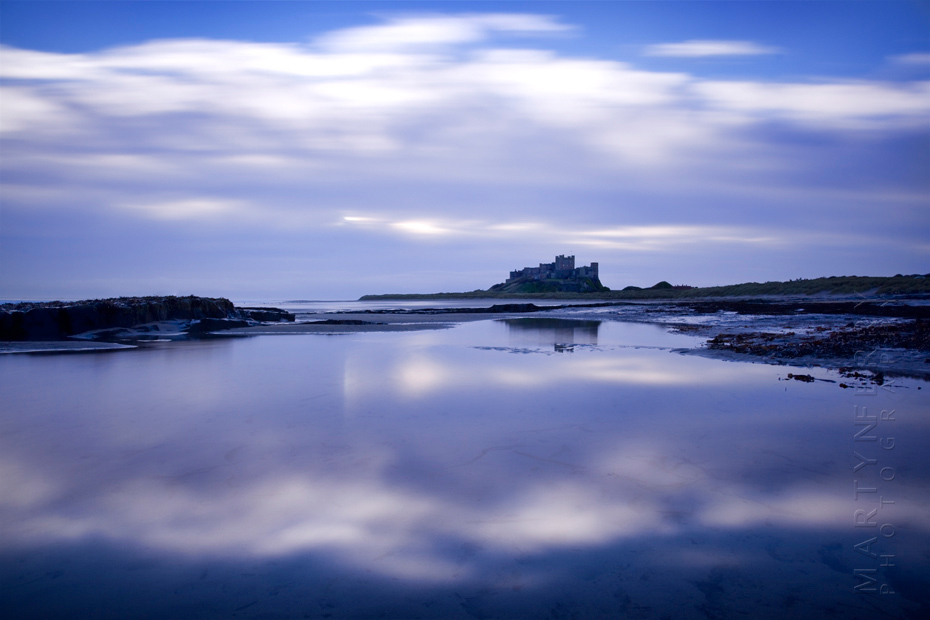 Clouds reflect in the landscape around the magnificent Bamburgh Castle at sunrise