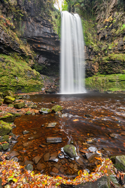 Autumn leaves in the foreground of Henrhyd Falls in Wales